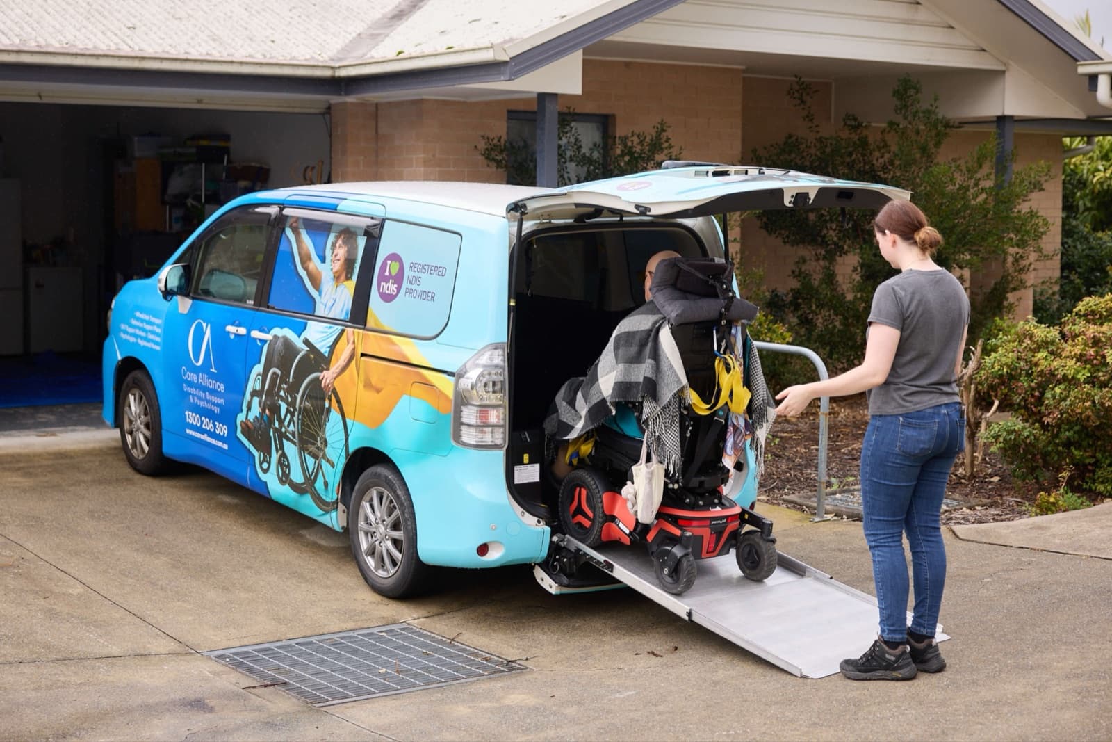 A Care Alliance support worker assisting a participant using a powered wheelchair