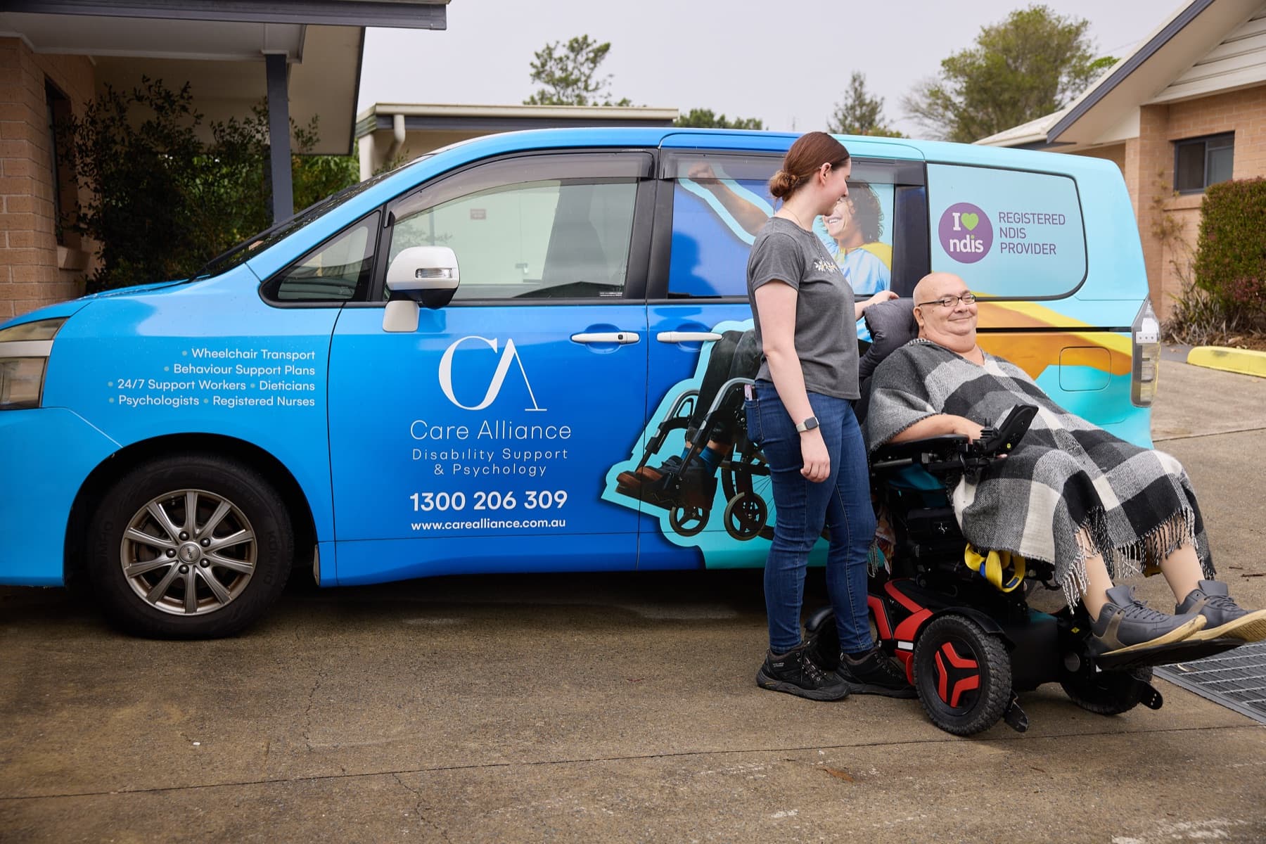A Care Alliance support worker with a participant beside a wheelchair-accessible van at his home